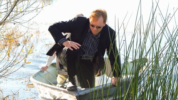 Ein Mann in Anzug steigt aus einem kleinen Boot am Ufer eines Sees.