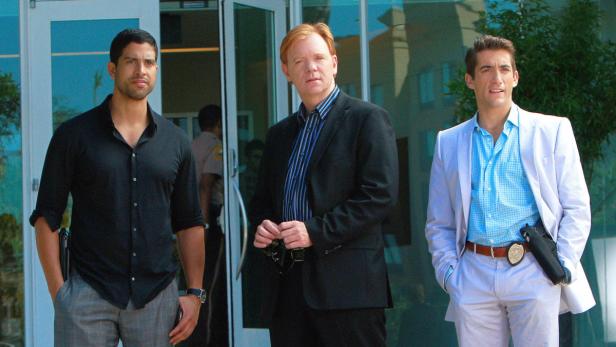 Drei Männer, vermutlich Polizisten, stehen vor einem Gebäude.