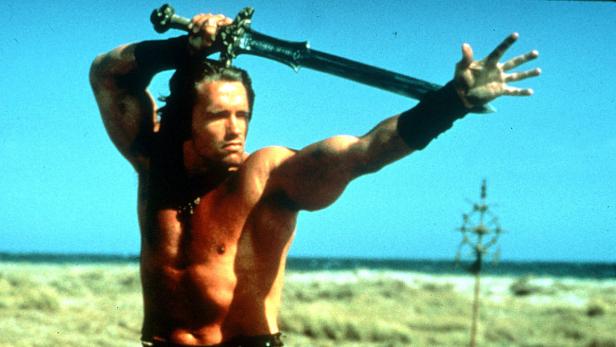 Arnold Schwarzenegger als Conan schwingt ein Schwert über seinem Kopf.