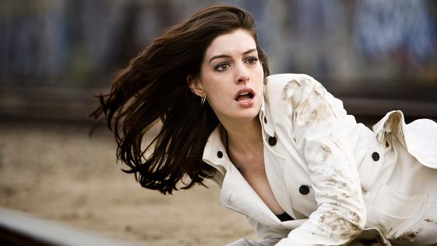 Anne Hathaway in einem schmutzigen, weißen Mantel blickt erschrocken zur Seite.