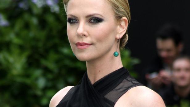 Charlize Theron mit dunklem Augen-Make-up und grünen Ohrringen.