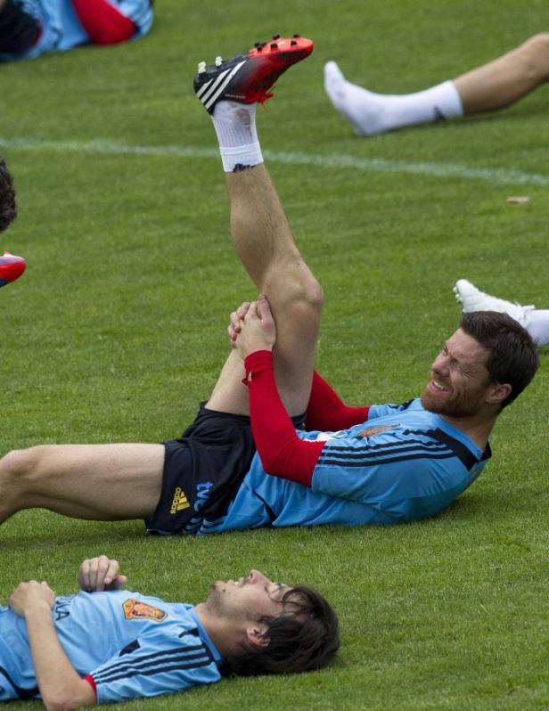 Ein Fußballspieler dehnt sich auf dem Rasen, während ein anderer daneben liegt.