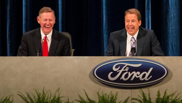Zwei Männer sitzen lachend vor einem Ford-Logo auf einer Bühne.