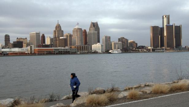 Ein Mann joggt am Ufer mit der Skyline von Detroit im Hintergrund.