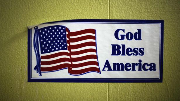 Ein Aufkleber mit der amerikanischen Flagge und dem Text „God Bless America“ an einer Wand.