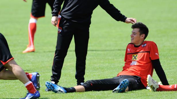 Ein Fußballspieler sitzt auf dem Rasen, während ein Trainer ihn berührt.