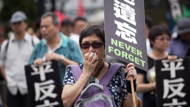 Eine Frau mit einem Schild „Never Forget“ demonstriert mit anderen Menschen.