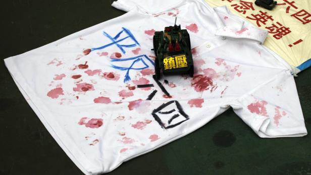 Ein T-Shirt mit roter Farbe, chinesischen Schriftzeichen und einem Spielzeugpanzer als Symbol für das Tian’anmen-Massaker.