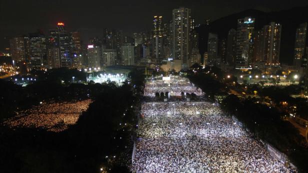 Eine große Menschenmenge versammelt sich nachts in Hongkong vor der Skyline.