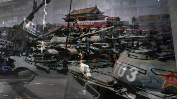 Ein Mann steht vor einem Foto von Panzern und dem Tiananmen-Platz.