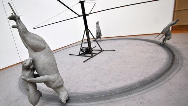 Eine Installation mit Tierfiguren, die an einem sich drehenden Gestell befestigt sind und Spuren auf dem Boden hinterlassen.
