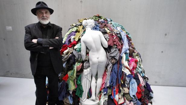 Ein Mann mit Hut steht neben einer Skulptur, die mit Kleidung bedeckt ist.