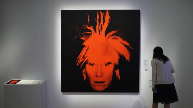 Eine Frau betrachtet ein Porträt von Andy Warhol in leuchtendem Orange.