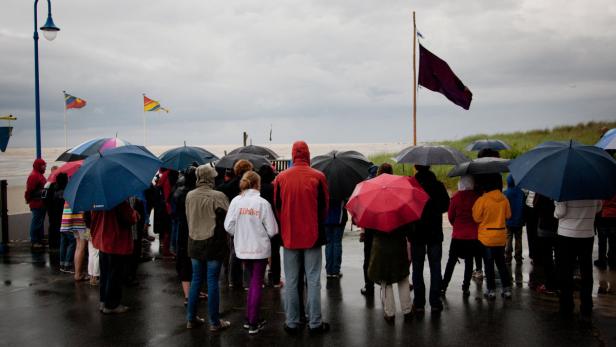 Eine Gruppe von Menschen steht mit Regenschirmen am Strand bei regnerischem Wetter.