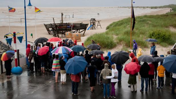 Eine Menschenmenge mit Regenschirmen steht an einem regnerischen Tag am Strand.