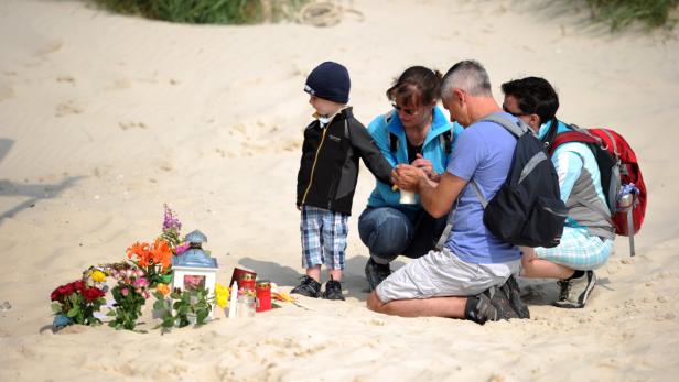 Eine Familie gedenkt an einem kleinen, mit Blumen geschmückten Denkmal am Strand.