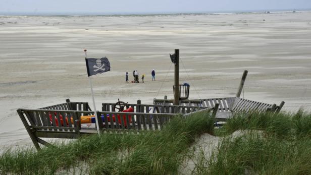 Ein hölzernes Spielschiff mit Piratenflagge steht am Strand.