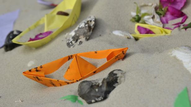 Mehrere Papierboote liegen im Sand.