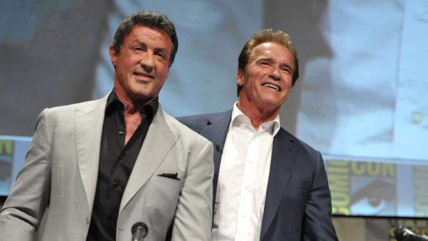 Sylvester Stallone und Arnold Schwarzenegger posieren zusammen auf einer Bühne.