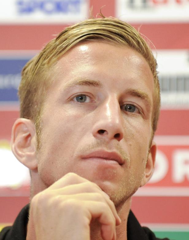 Ein Mann mit blonden Haaren und blaugrünen Augen blickt nachdenklich in die Ferne.