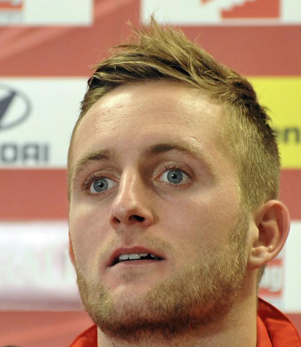 Ein Mann mit blonden Haaren und Bart schaut aufmerksam zur Seite.