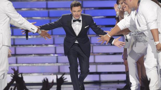 Ryan Seacrest geht auf einer Bühne an jubelnden Menschen vorbei.