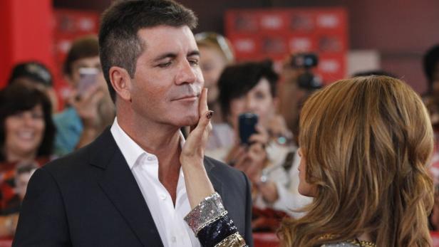 Simon Cowell wird von einer Frau berührt, während im Hintergrund Menschen mit Handys stehen.