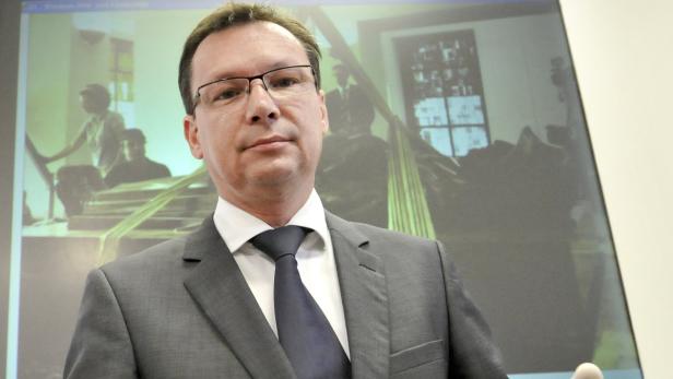 Ein Mann mit Brille und Anzug steht vor einer Leinwand mit einem Schwarzweißbild.
