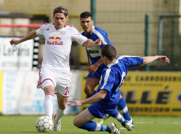 Ein Fußballspieler in Weiß mit der Nummer 24 am Ball, verfolgt von zwei Gegenspielern in Blau.