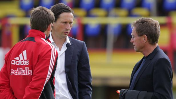 Drei Männer in Anzügen unterhalten sich auf einem Sportplatz.