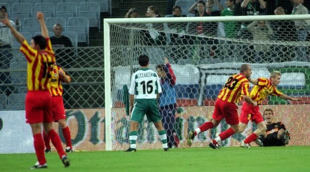 Fußballspieler in rot-gelben Trikots jubeln vor dem Tor, während ein Spieler in Grün enttäuscht ist.