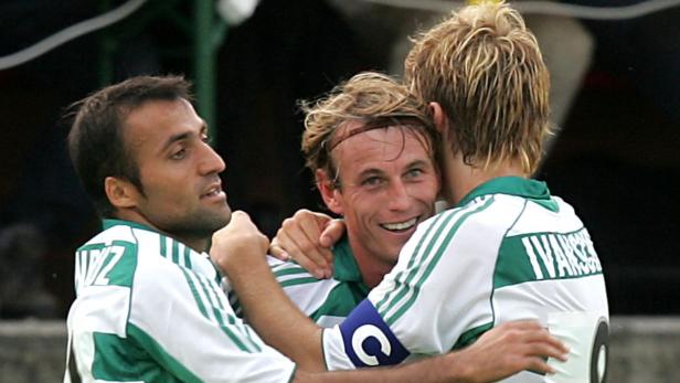 Drei Fußballspieler in grün-weißen Trikots umarmen sich und feiern.