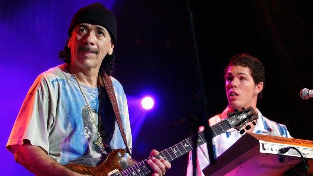 Carlos Santana spielt Gitarre während eines Konzerts, begleitet von einem Keyboardspieler.