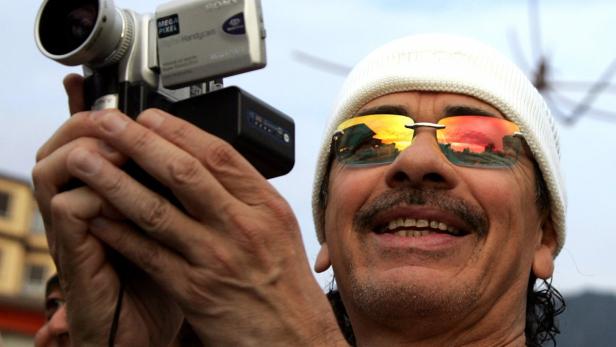 Carlos Santana filmt mit einer kleinen Videokamera, in dessen Sonnenbrille sich ein Sonnenuntergang spiegelt.