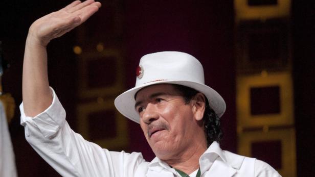 Carlos Santana mit weißem Hut und erhobener Hand.
