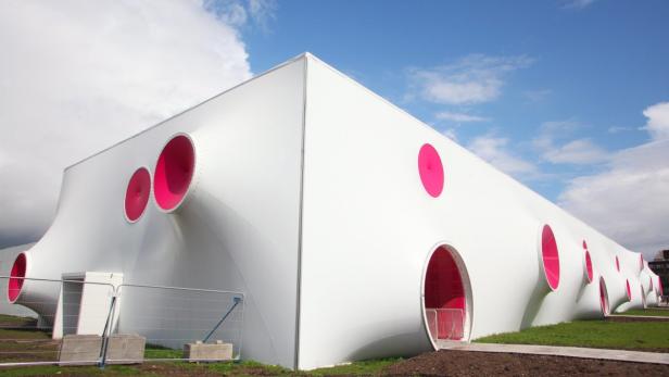 Ein weißes, ungewöhnliches Gebäude mit pinkfarbenen, runden Öffnungen unter einem blauen Himmel.