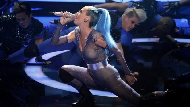 Katy Perry tritt mit blauen Haaren und einem glitzernden Overall auf einer Bühne auf.