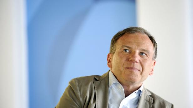 Ein Mann in einem hellbraunen Sakko und hellblauem Hemd blickt nach oben.