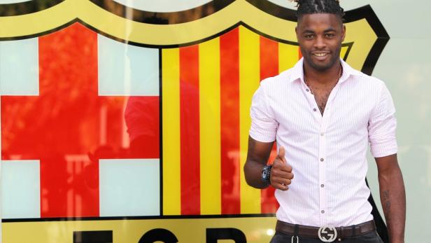 Ein Mann mit Dreadlocks posiert vor dem Vereinswappen des FC Barcelona und zeigt den Daumen nach oben.