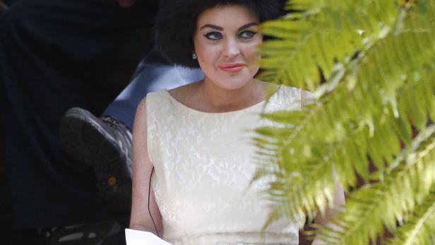 Lindsay Lohan in einem hellen Kleid, teilweise von Farnen verdeckt.