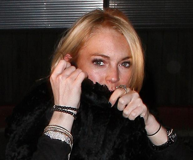 Lindsay Lohan hält einen schwarzen Pelzmantel vor ihr Gesicht.