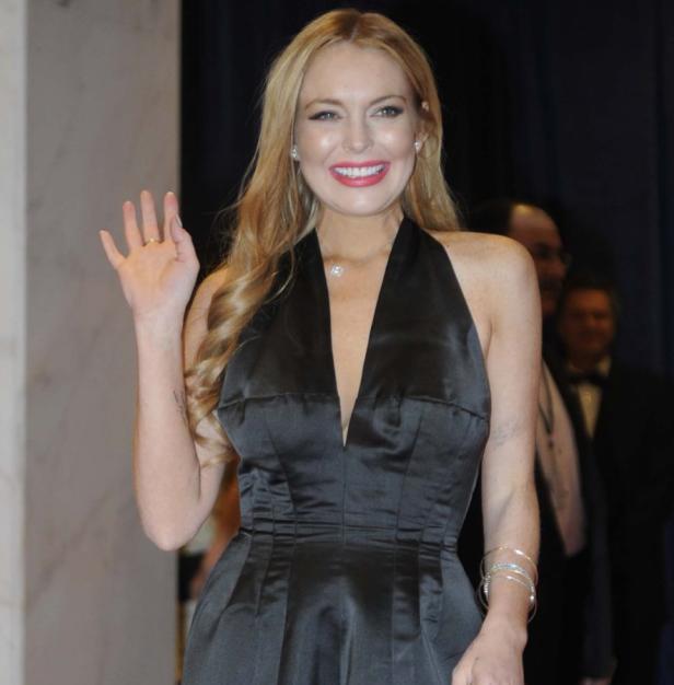 Lindsay Lohan in einem schwarzen Kleid winkt in die Kamera.