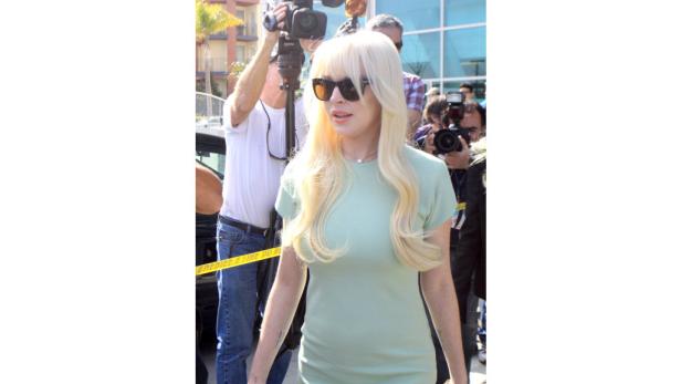 Lindsay Lohan mit blonder Perücke und Sonnenbrille, umringt von Fotografen.