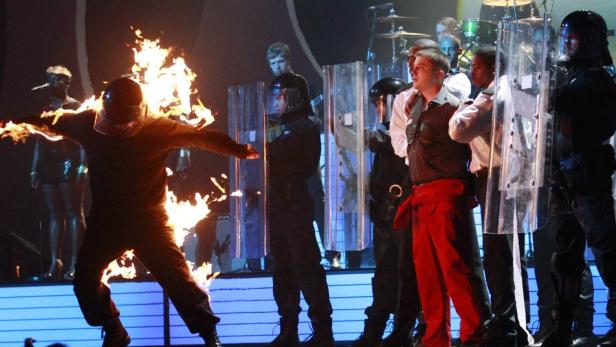 Ein Mann steht in Flammen vor einer Reihe von Polizisten mit Schutzschilden.