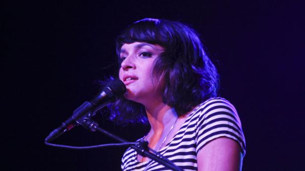 Eine Sängerin mit dunklen Haaren singt in ein Mikrofon.
