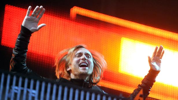 David Guetta legt bei einem Konzert auf und streckt die Hände in die Luft.