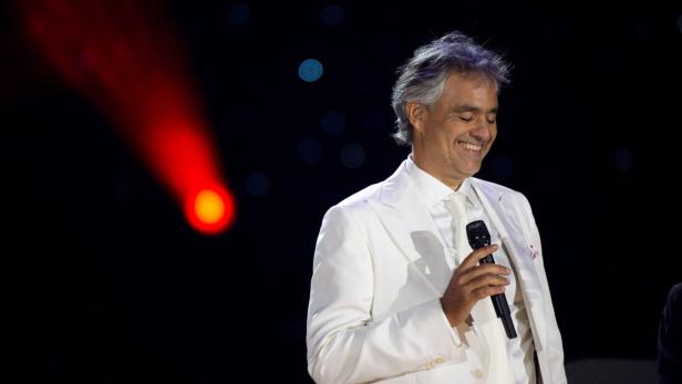 Andrea Bocelli lächelt mit einem Mikrofon in der Hand auf einer Bühne.