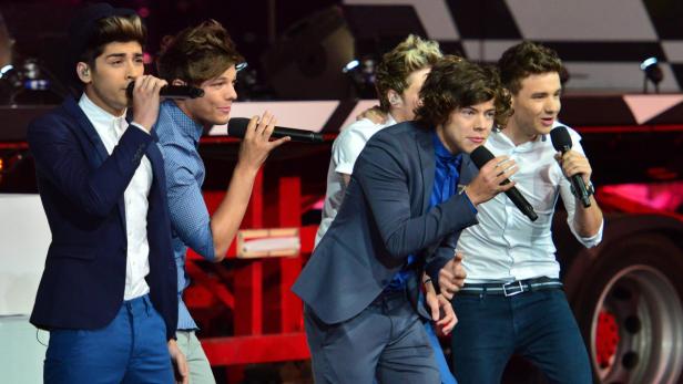 Die Band One Direction tritt auf einer Bühne mit Mikrofonen auf.