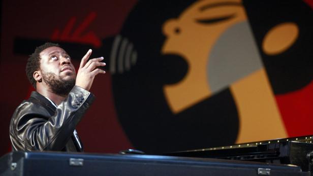 Ein Mann mit Bart spielt Klavier vor einem farbenfrohen Hintergrund.