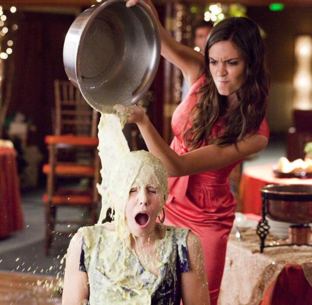 Eine Frau schüttet einer anderen Frau eine Schüssel mit einer unbekannten Substanz über den Kopf.